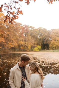 a man and woman standing next to each other in front of a lake