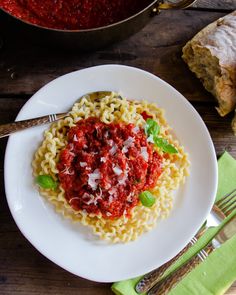 a white plate topped with pasta and sauce next to silverware on top of a wooden table