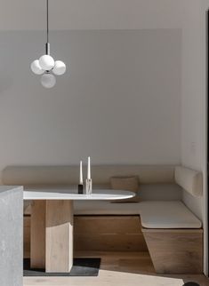 a white table and bench in a room with wooden flooring on one side and light fixture hanging from the ceiling