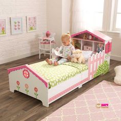 a toddler sitting on a bed with a book shelf and stuffed animals in it