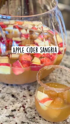 two glasses filled with liquid sitting on top of a counter next to a bowl full of fruit