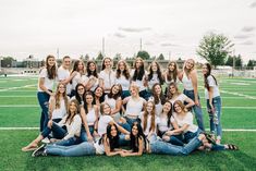 a group of young women posing for a photo on a football field in white shirts and jeans