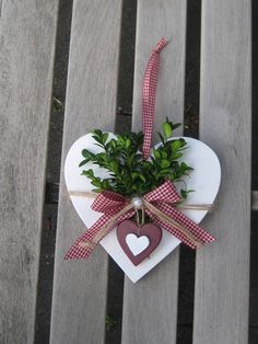 a heart shaped box with greenery tied to it on a wooden bench, next to a potted plant