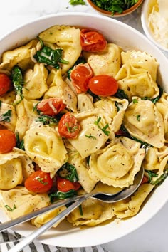 a white bowl filled with pasta, tomatoes and spinach on top of a table