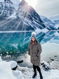 a woman standing in the snow next to a body of water with mountains in the background