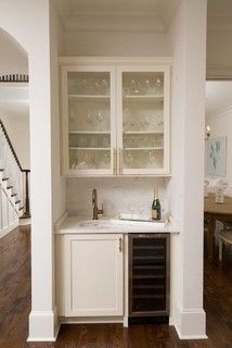 a kitchen with white cabinets and wine glasses on the top shelf in front of it