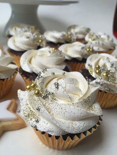 some cupcakes with white frosting and gold decorations on them are sitting on a table