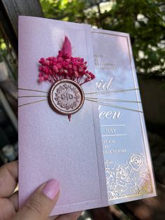 a person holding up a pink and gold wedding card with flowers on the inside of it