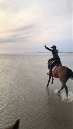 a woman riding on the back of a brown horse across a sandy beach next to water