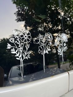 three flowers are drawn on the side of a car's glass window, with trees in the background