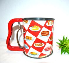 a red and white checkered coffee mug next to a green plant