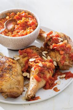 two pieces of chicken on a plate with a bowl of tomato sauce and almonds