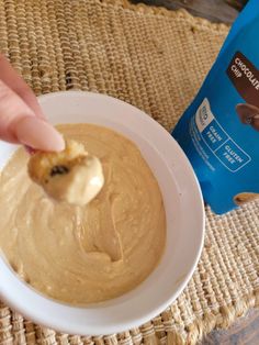 a person dipping something into a bowl with peanut butter on it next to a bag of peanuts