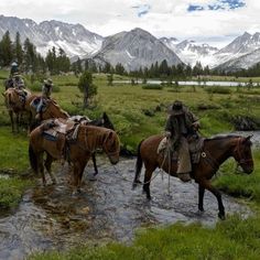 several people riding horses across a stream in the mountains