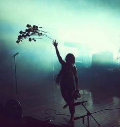 a woman standing on top of a wooden floor next to a tree in the fog