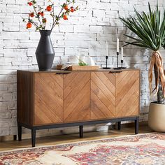 a sideboard with flowers and candles on it in front of a white brick wall