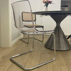 a glass table with two chairs and a vase on the top is sitting in front of it