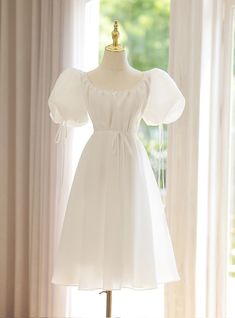 a white dress on a mannequin stand in front of a window with curtains