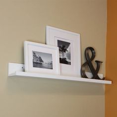 two pictures are hanging on the wall above a shelf with a pair of black and white photos