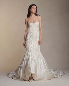 a woman in a white wedding dress standing on a beige background with her head turned to the side