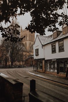 an empty street with buildings in the background and snow falling on the ground around it