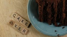 a blue plate topped with a piece of chocolate cake next to scrabble letters