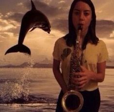 a woman is playing the saxophone with a dolphin jumping in the air behind her and another dolphin leaping out of the water