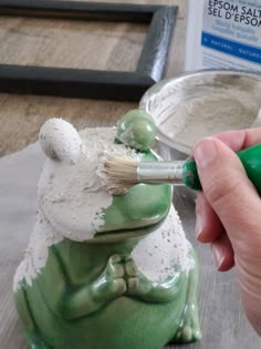 a person is painting a frog statue with green paint