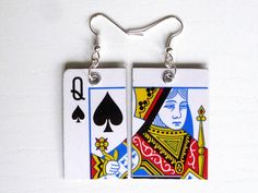 two playing cards are hanging from silver earwires on a white background with the image of queen and ace