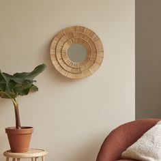 a living room with a chair, potted plant and round mirror on the wall