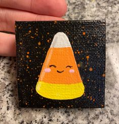 a hand holding a small piece of art with a candy corn on it's face