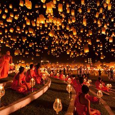 people are sitting on the ground with lanterns in the sky