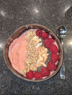 a bowl filled with fruit and granola on top of a table next to a spoon