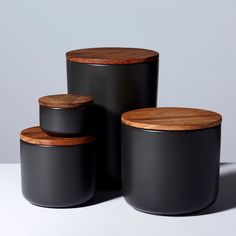 three black canisters with wooden lids on a white surface