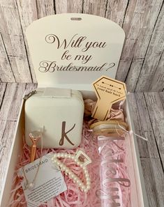 an open box with personal items inside it on a wooden floored surface and the words will you be my bridesmaid written in white