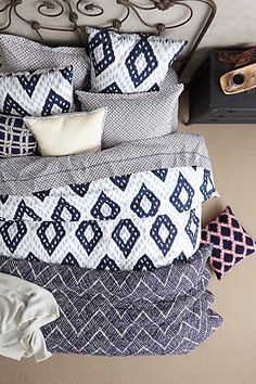 a bed with blue and white pillows on top of it next to an iron headboard