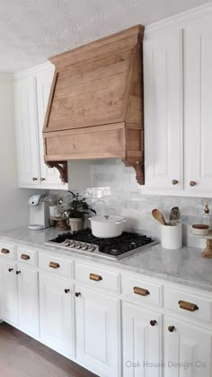 a kitchen with white cabinets and wood accents on the hood over the stove, along with wooden utensils