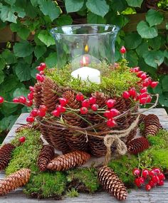 a candle is lit in a glass vase filled with red berries and pine cones