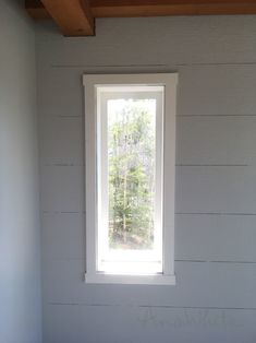 a window in the corner of a room with white walls and wood beams on the ceiling