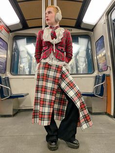 a woman dressed in plaid clothing standing on a train