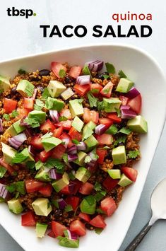 a white bowl filled with taco salad on top of a table next to a spoon