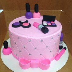 a pink cake decorated with cosmetics and makeup products in a box on top of a table