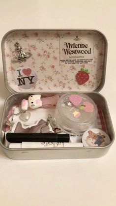 an open tin with various items in it on a white tableclothed surface, including a pen and keychain