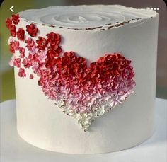 a white cake with red and pink flowers on it's icing is decorated in the shape of a heart