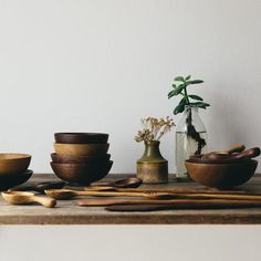 wooden bowls and spoons sit on a table next to a vase with flowers in it