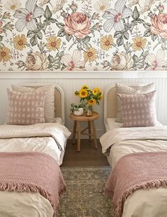 two twin beds in a room with floral wallpaper on the walls and side tables