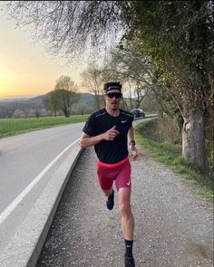 a man running down a road next to a tree and grass covered hillside in the background