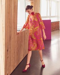 a woman in a pink dress is standing by a wall and looking at the floor