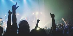 a group of people at a concert with their hands up in the air and lights on