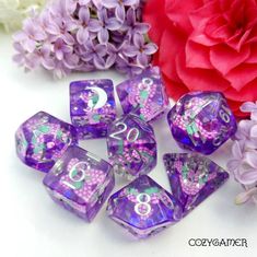 purple and green dice with numbers on them next to some pink flowers, one red flower